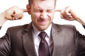 A man in a suit plugs his ears with his fingers trying to relieve and clear his ear canals